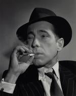 Actor Humphrey Bogart in pinstripe suit and fedora smoking a cigarette squinting through the smoke.