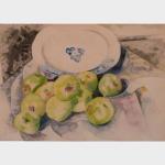 Green apples piled in front of a white plate with blue pattern. 