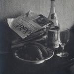 Black and white still life of bottle, newspapers, wine glass, and bananas on a plate. 