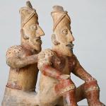 Two ceramic sitting figures joined - one behind the other.
