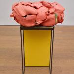 Coral colored ceramic sculpture that looks like overlapping tongues on a yellow pedestal.