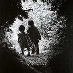 Black and white photo of two young children walking in a forest.